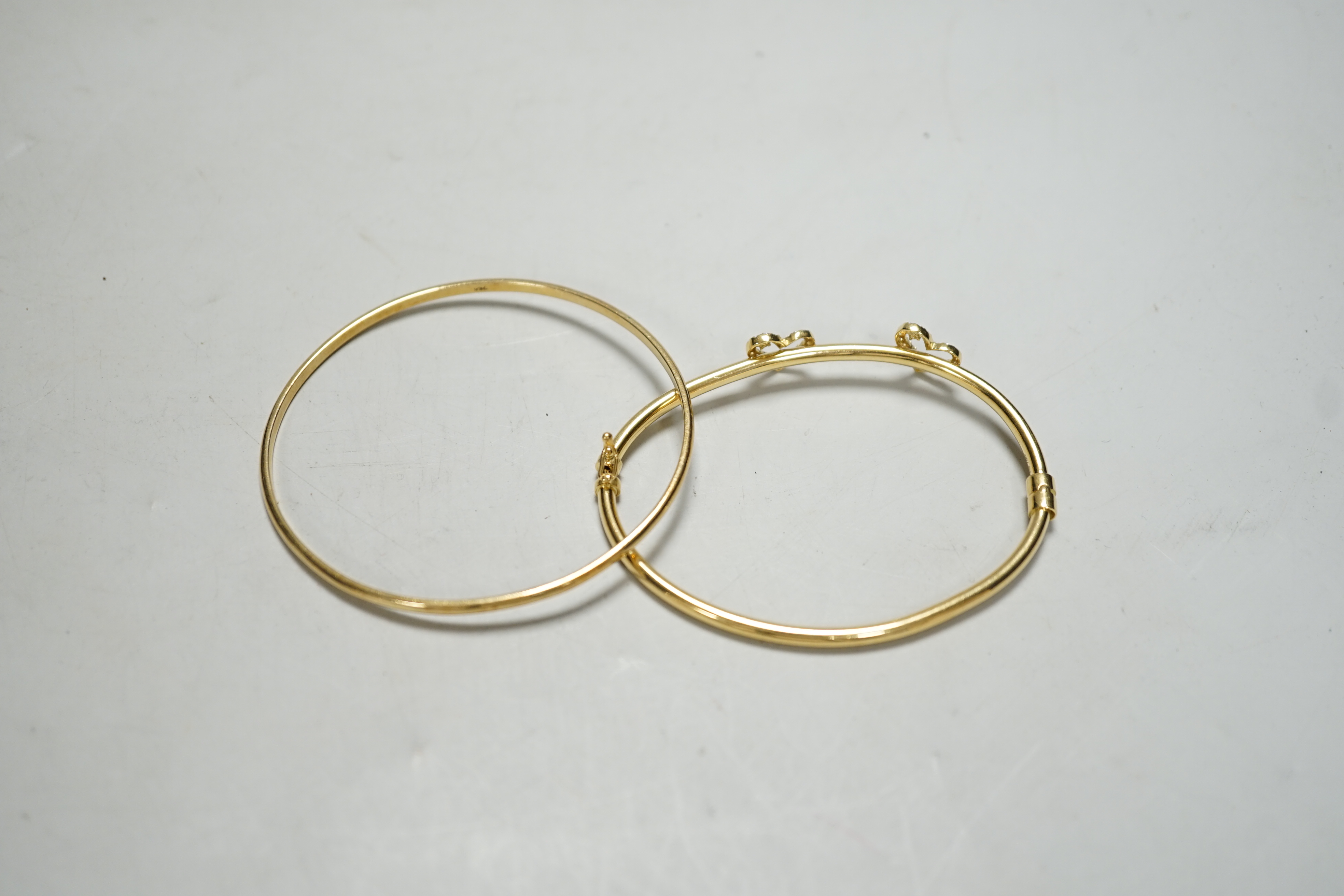 Two modern 750 yellow metal hinged bangles, one with diamond set twin hearts motif